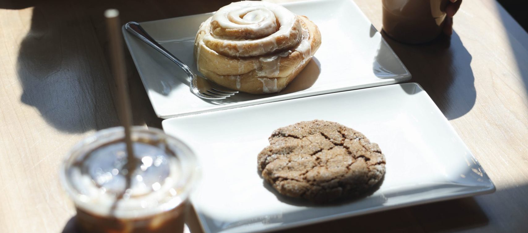 Two iced coffees, a cinnamon roll, and a cookie on a sunlit café table