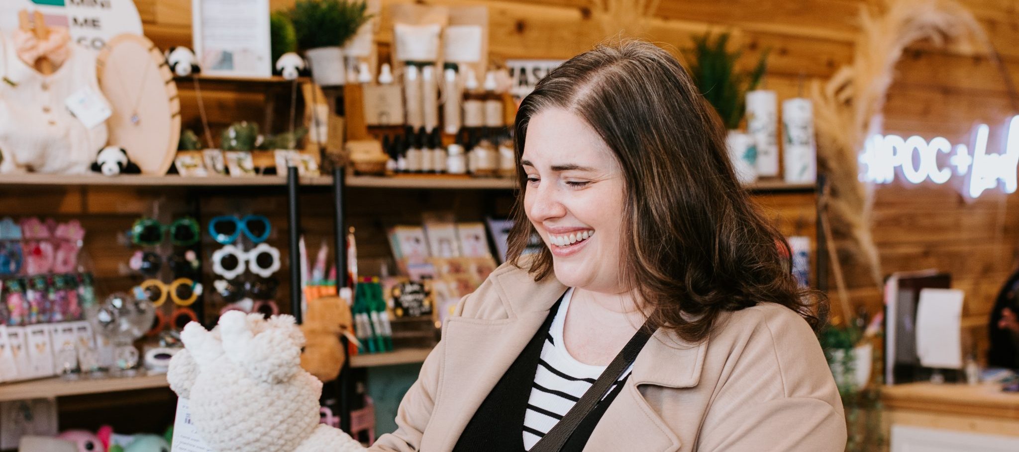 Women holding hand made cow plush in front of shelves in a store with shop items on them.